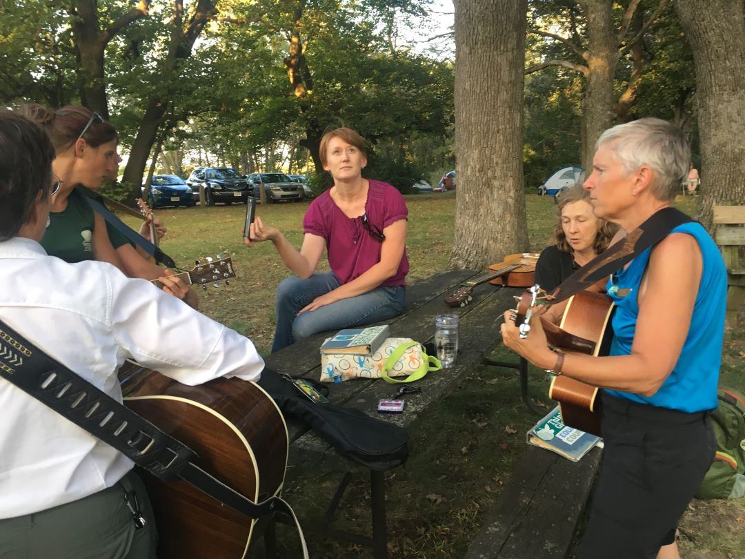 Group of women tune acoustic guitars in a circle