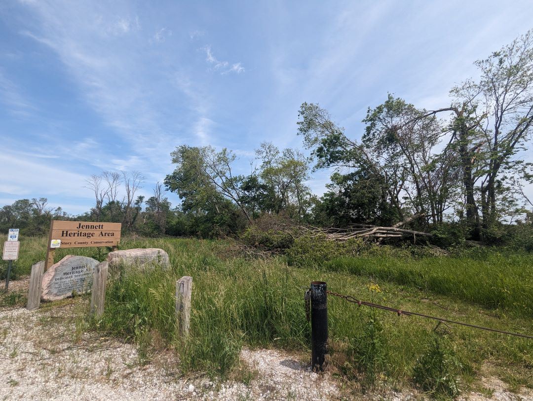 Jennnett Heritage Area sign at corner of parking area, with downed trees visible from tornado