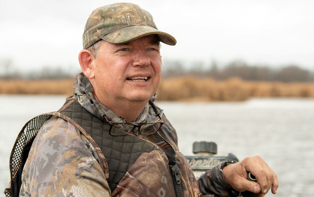 Older white male with camouflage hat looks into distance while on a waterfowl hunt